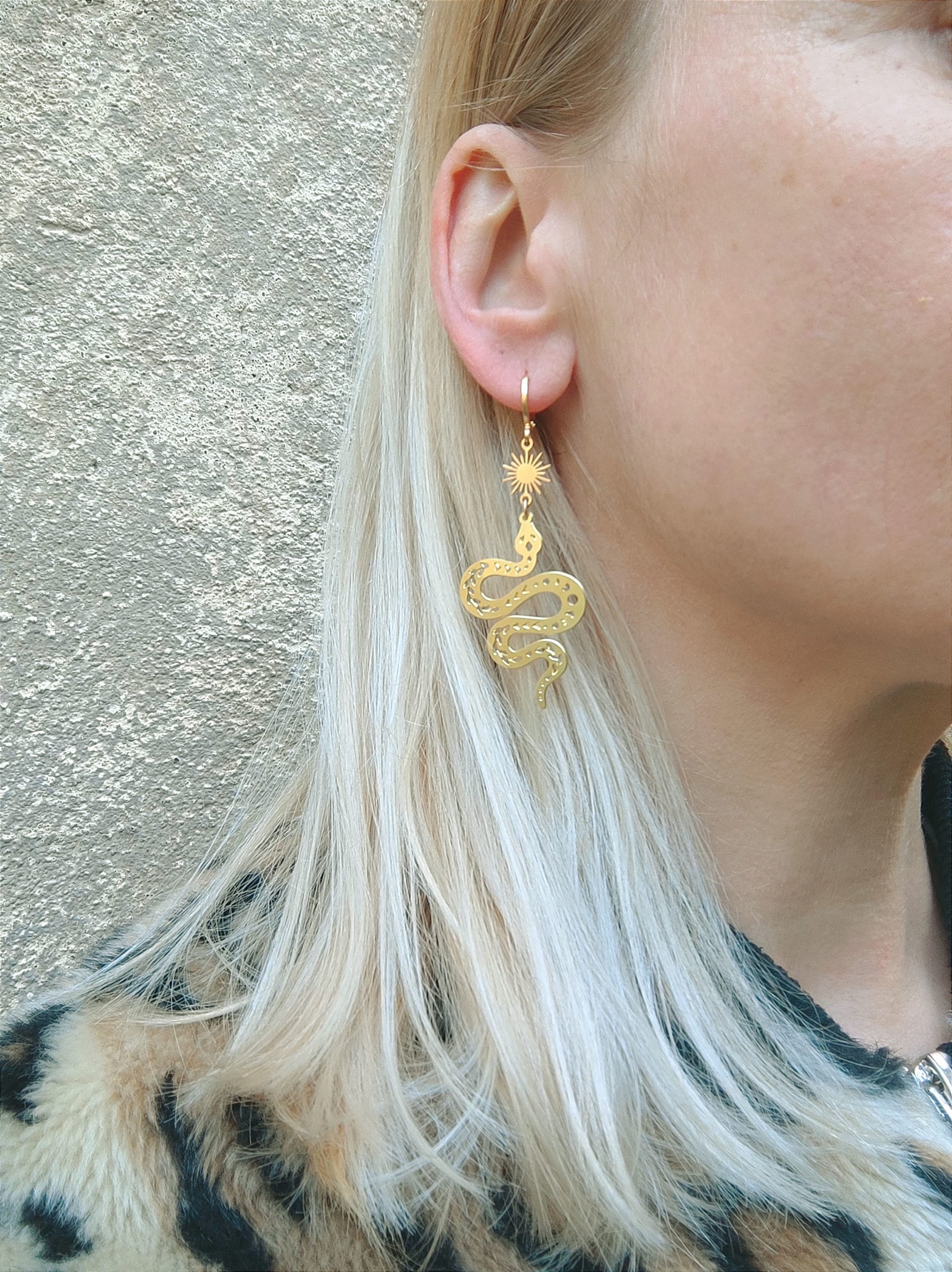 Femme qui porte des boucles d'oreilles dorées serpent